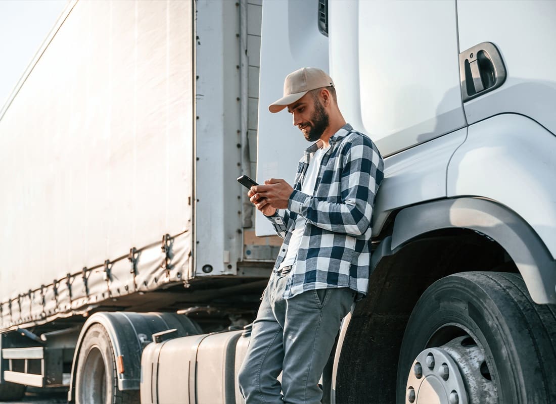 About Our Agency - Young Truck Driver Using His Phone While Leaning by the Vehicle